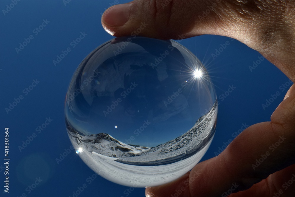 Mountains in the snow through a glass ball in your hand. Winter landscape through a glass ball in your hand