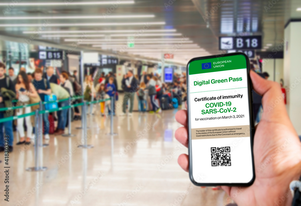The digital green pass of the european union with the QR code on the screen of a mobile held by a hand with a blurred airport in the background
