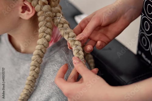 The hairdresser braids the girl in braids in the beauty salon. Close-up