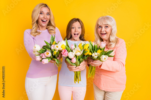 Photo of nice impressed blond red hair grand mom daughter give flowers wear pastel cloth isolated on yellow color background