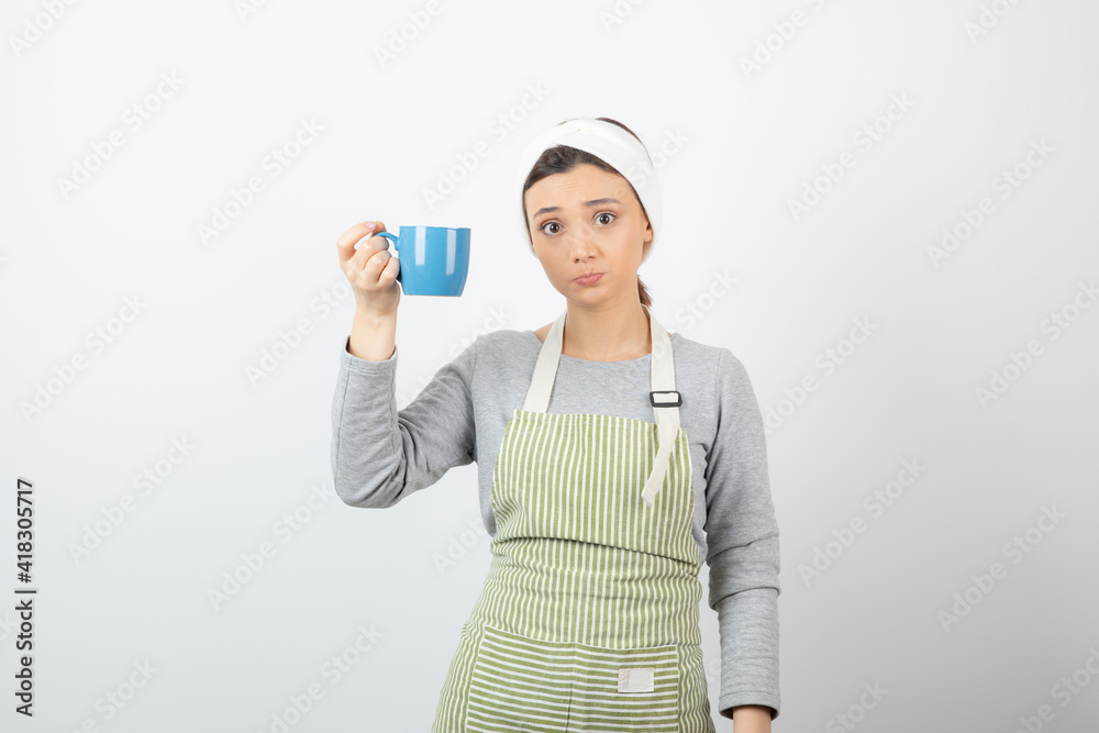 Image of a pretty young woman in apron holding a blue cup Image of a pretty young woman in apron holding a blue cup