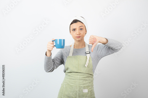 Image of a cute young woman in apron with a blue cup showing a thumb down