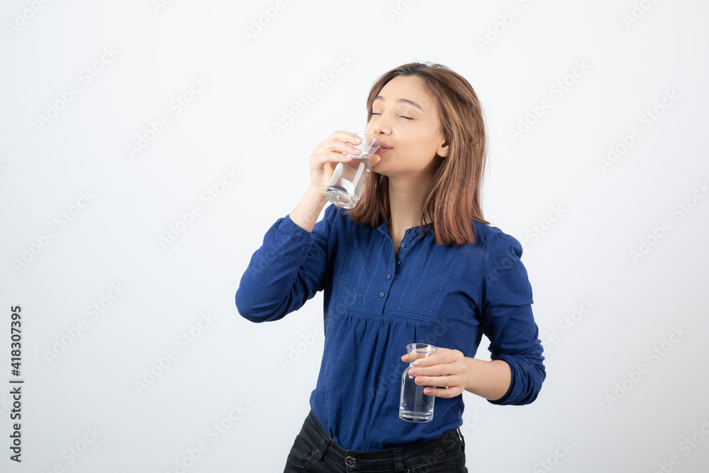 Young woman in blue blouse drinking glass of water over white wall Young woman in blue blouse drinking glass of water over white wall