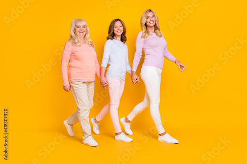 Full size profile photo of optimistic three woman grand mom daughter go hold hands wear pastel cloth isolated on yellow background