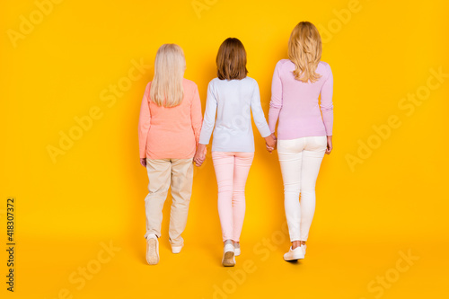 Full size back photo of optimistic three woman grand mom daughter go wear pastel cloth isolated on yellow background