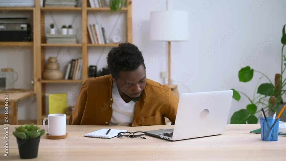 Man working with computer remotely and sitting at desk in home office spbas. Young businessman puts on glasses, sits down at table and looks at laptop screen in light room. Millennial guy uses Man working with computer remotely and sitting at desk in home office spbas. Young businessman puts on glasses, sits down at table and looks at laptop screen in light room. Millennial guy uses