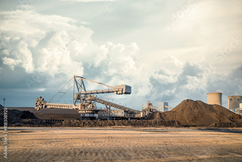 Bucket wheel machine large surface mining excavator at UK power station working in open cast heaps and piles of coal in coalfield dramatic cloud sky and cooling towers photo