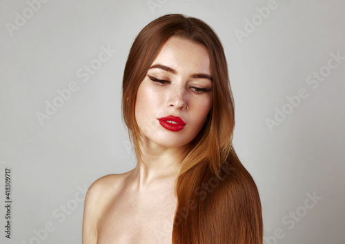 Long healthy straight hair. Beauty woman with long shiny brown hair red lips and nose piercing. Model brunette portrait isolated on a gray background.