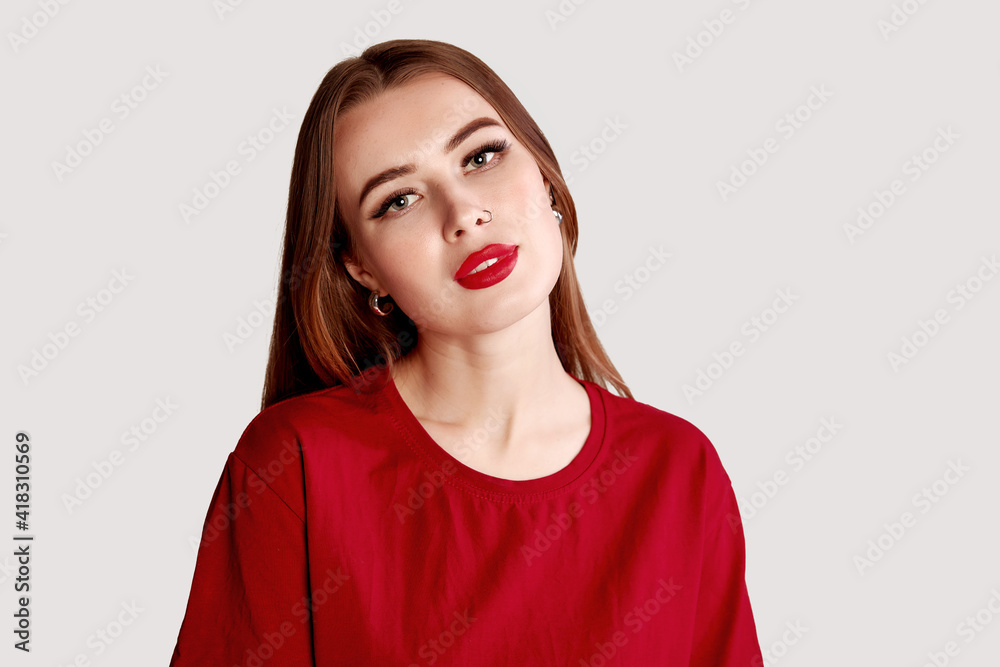 Beautiful face of young adult woman with nose earring and clean fresh skin. Portrait of cute brunette with red lips and nose piercing posing in a red t-shirt on gray Beautiful face of young adult woman with nose earring and clean fresh skin. Portrait of cute brunette with red lips and nose piercing posing in a red t-shirt on gray