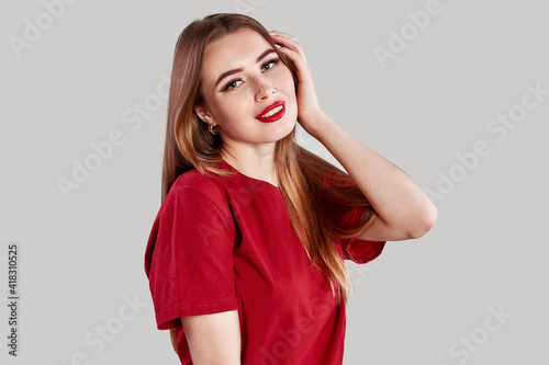 Beautiful face of young adult woman with nose earring and clean fresh skin. Portrait of cute brunette with red lips and nose piercing posing in a red t-shirt on gray
