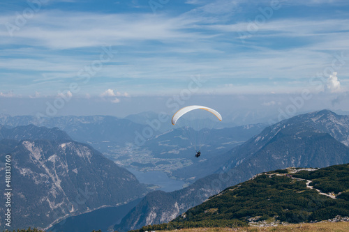 Man with white-and-yellow parachute hovers over Mount Krippenstein in upper Austria, enjoying view of valley and rest of the Austrian alps. Ideal sunny weather without gusty winds for paragliding