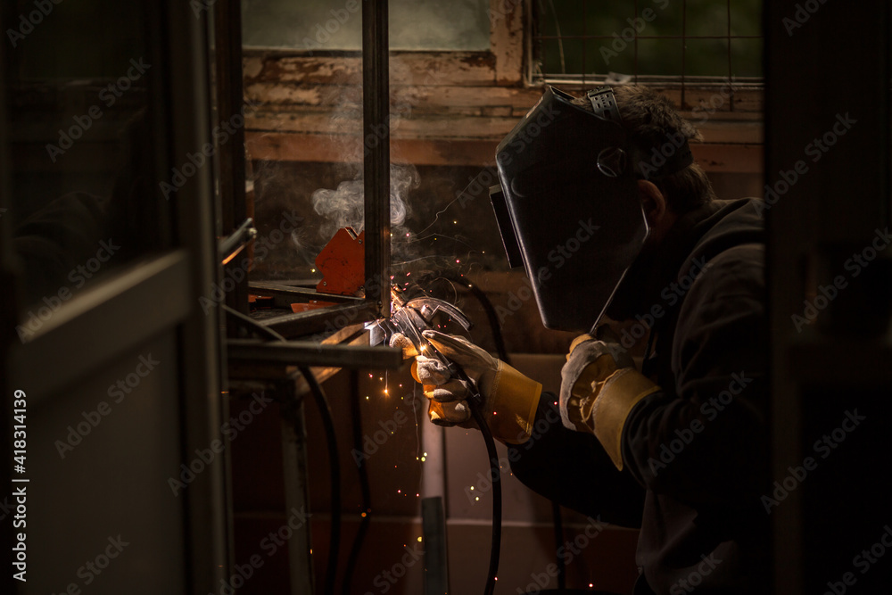 a welder in a welding mask, gloves welds metal with a welding machine and an electrode in his hand, sparks fly, a beautiful glow, bokeh, orange light on a black background, a flash of light and smoke a welder in a welding mask, gloves welds metal with a welding machine and an electrode in his hand, sparks fly, a beautiful glow, bokeh, orange light on a black background, a flash of light and smoke