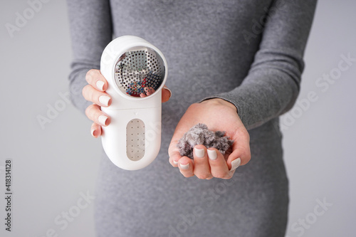 Female hand with modern fabric shaver and clothes on color background