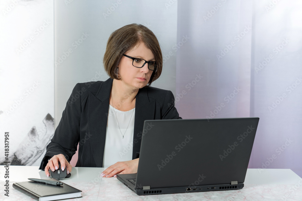 A brunette bussiness woman in glasses in a black jacket works on the computer in the office A brunette bussiness woman in glasses in a black jacket works on the computer in the office