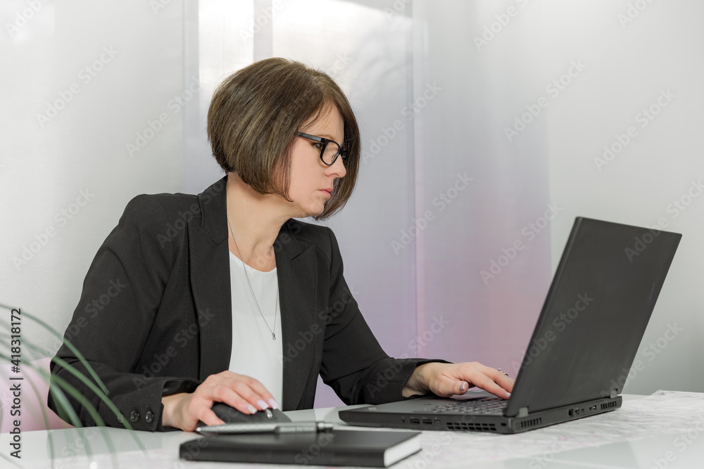 A brunette bussiness woman in glasses in a black jacket works on the computer in the office A brunette bussiness woman in glasses in a black jacket works on the computer in the office