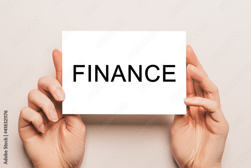 Female hands hold card paper with text FINANCE on a yellow background. Business and finance concept Female hands hold card paper with text FINANCE on a yellow background. Business and finance concept