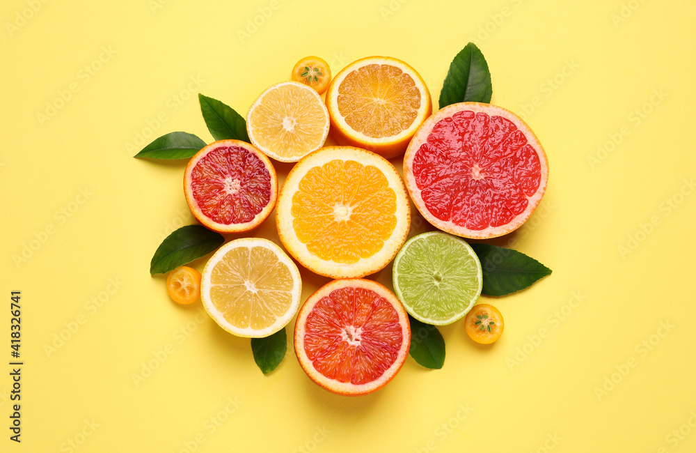 Fresh juicy citrus fruits with green leaves on light yellow background, flat lay Fresh juicy citrus fruits with green leaves on light yellow background, flat lay