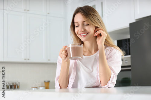 Young woman with glass cup of chocolate milk in kitchen