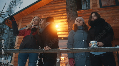 Best friends having fun on winter vacation. Drinking hot beverage in front of the wooden house on the mountain. High quality photo