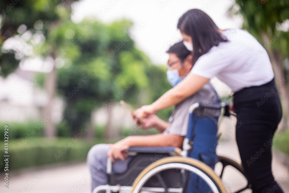 Blurred disabled man on wheelchair and sister walking in the park Blurred disabled man on wheelchair and sister walking in the park