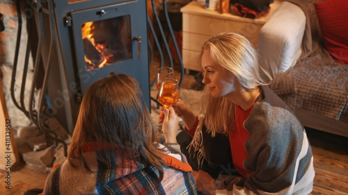 Foto two young women, lesbian couple relaxing near the fireplace and drinking wine in the cozy home