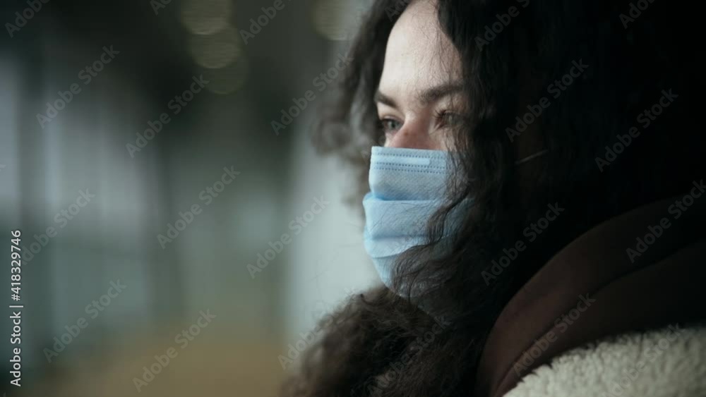 portrait of a girl in a medical mask in street clothes on a city street or at the airport. Wind movement, breath feeling. Sad eyes and loneliness portrait of a girl in a medical mask in street clothes on a city street or at the airport. Wind movement, breath feeling. Sad eyes and loneliness