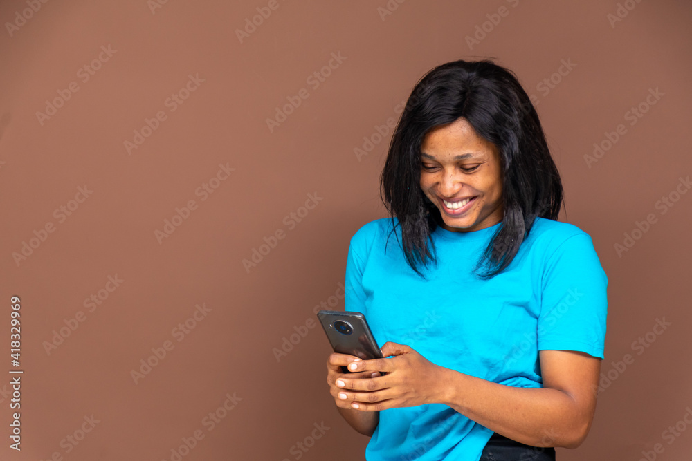 beautiful young african woman smiling while using her phone, standing in front of a plain brown background beautiful young african woman smiling while using her phone, standing in front of a plain brown background