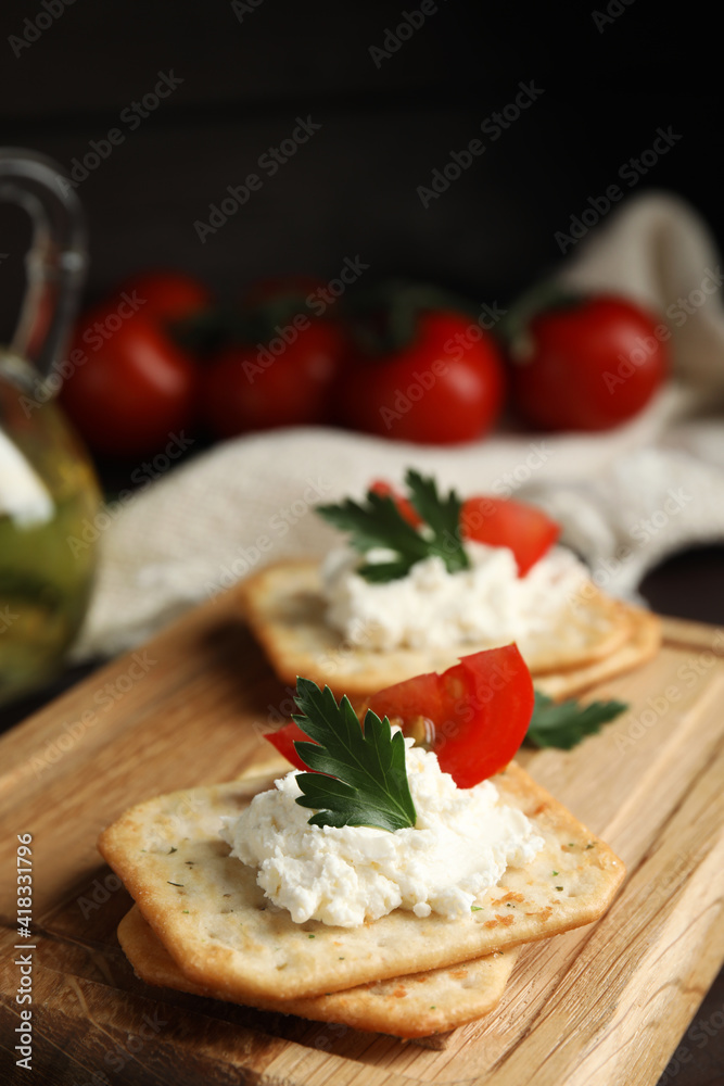 Delicious crackers with cream cheese, tomato and parsley on wooden board, closeup Delicious crackers with cream cheese, tomato and parsley on wooden board, closeup