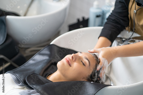 Beautiful Caucasian women feel relax and comfortable while getting hair wash with shampoo and massage. Hair salon studio with hair stylish, beauty and fashion concept.