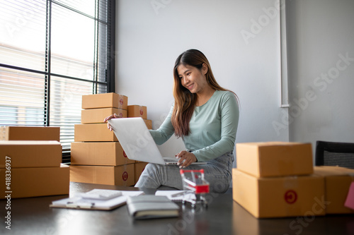 Young asian woman is entrepreneur work from home with online on notebook, online shopping, logistic and delivery, female is seller working on sofa, business SME