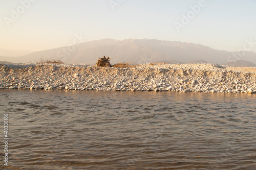 Calm river landscape with debris and a mountain in the background in a sunny day.