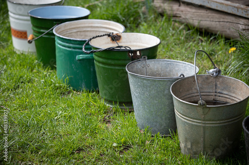 Many different buckets stand in a row to collect rainwater. Buckets of water stand on the grass in the garden next to the house. Village concept