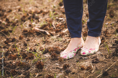 Closeup of a woman's legs in pumps and dark jeans on the ground. Sunny summer day outdoors. A woman walks in the park.
