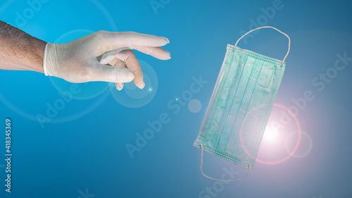 Futuristic banner with a hand in medical glove trying to get a face mask, design concept with copy space for text at gradient blue background and lens flare, details.