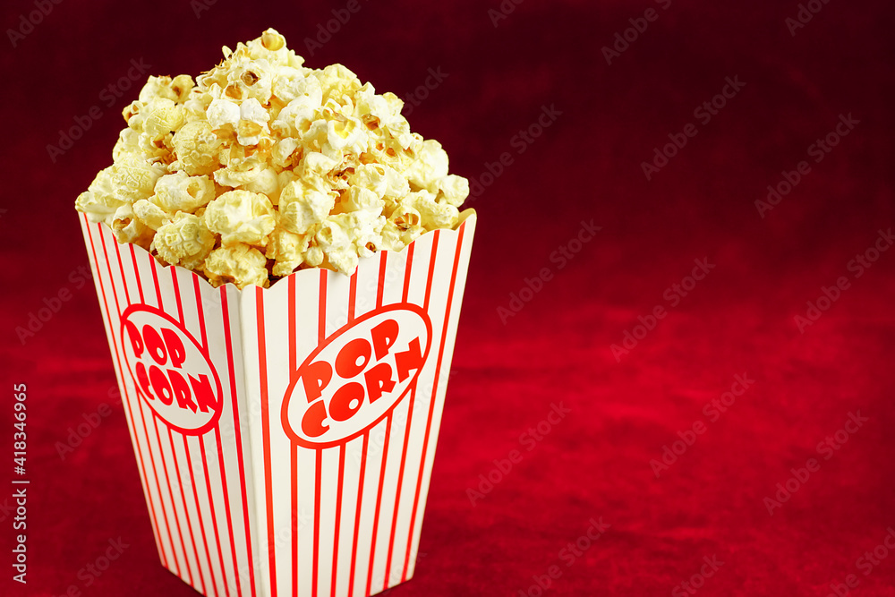 Full popcorn in a classic popcorn box on a red background.Popcorn spinning in circles around.
Full popcorn in a classic popcorn box on a red background.Popcorn spinning in circles around.