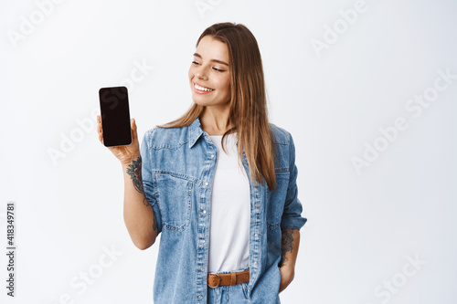 Φωτογραφία Stylish girl showing empty mobile phone screen and looking pleased, recommending
