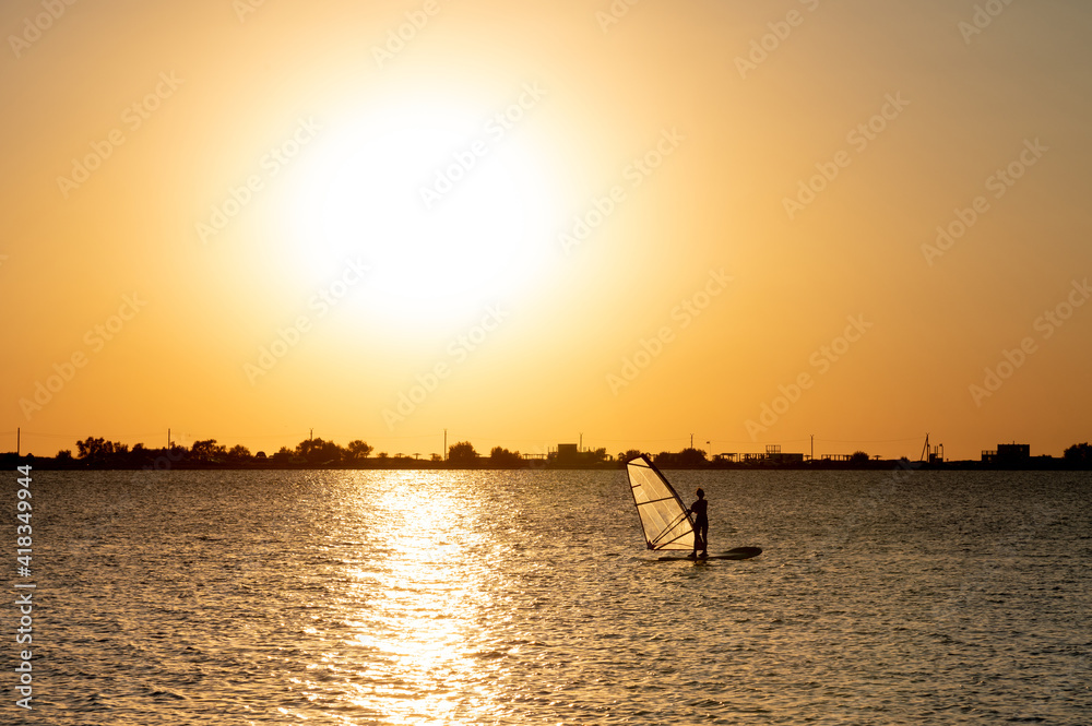 Woman windsurfer silhouette at lake sunset. Beautiful beach landscape. Summer water sports activities, recreation and travel concept
