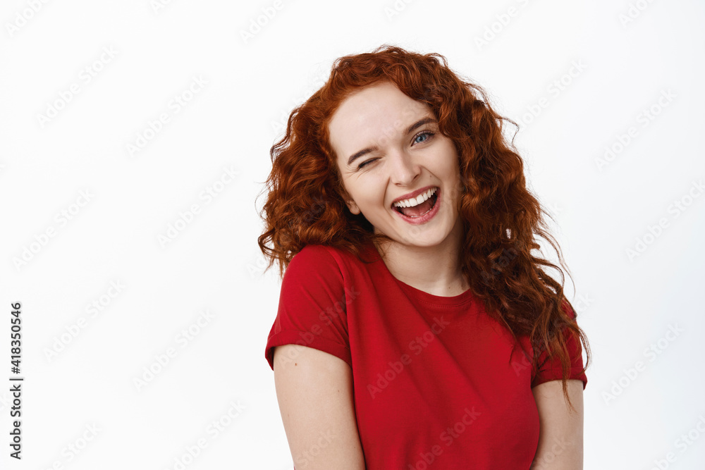 Close-up portrait of silly redhead girl with curly hairstyle, tilt head flirty and winking at camera coquettish, smiling relaxed and happy, standing in t-shirt against white background Close-up portrait of silly redhead girl with curly hairstyle, tilt head flirty and winking at camera coquettish, smiling relaxed and happy, standing in t-shirt against white background