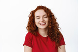 Close up portrait of dreamy redhead teen girl close eyes and smiling, feeling happiness and joy, dreaming about something, standing against white background