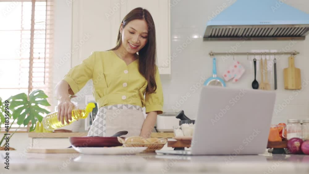 A beautiful Asian girl makes breakfast by looking at how to make it with her laptop computer with a happy face. At her own house A beautiful Asian girl makes breakfast by looking at how to make it with her laptop computer with a happy face. At her own house