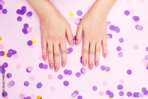 Elegant nude manicure on a pink background with confetti
