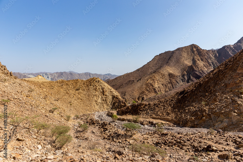 Hajar Mountains landscape in Hatta, United Arab Emirates, seen from a hiking trail, with harsh climate, dry, rocky mountain slopes and dwarf trees and bushes.