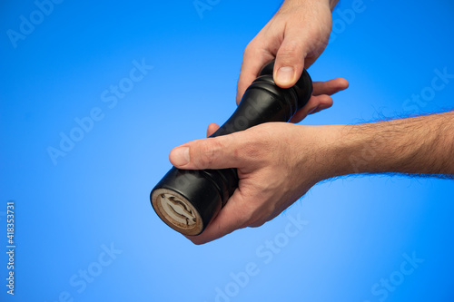 Wooden black pepper  grinder mill held by Caucasian male hands studio shot isolated on blue background photo