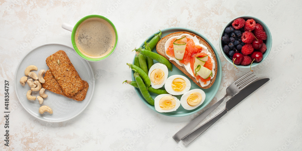 Healthy breakfast -  open sandwich with salmon and cucumber, boiled eggs, peas, coffee, biscuits, nuts and berries on a bright background. Top view.