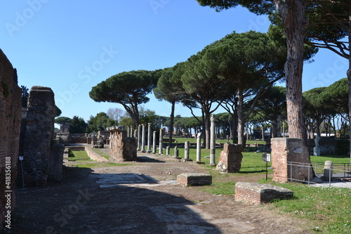 Ancient Roman Street in Ostia Antica with marble columns and old trees empty on a sunny day