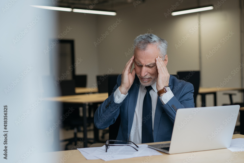Portrait of tired stressed businessman having headache sitting in office. Overwork concept
