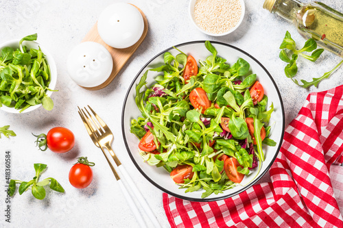 Green salad with arugula, lamb and tomatoes. Healthy vegan dish. Top view at white table.