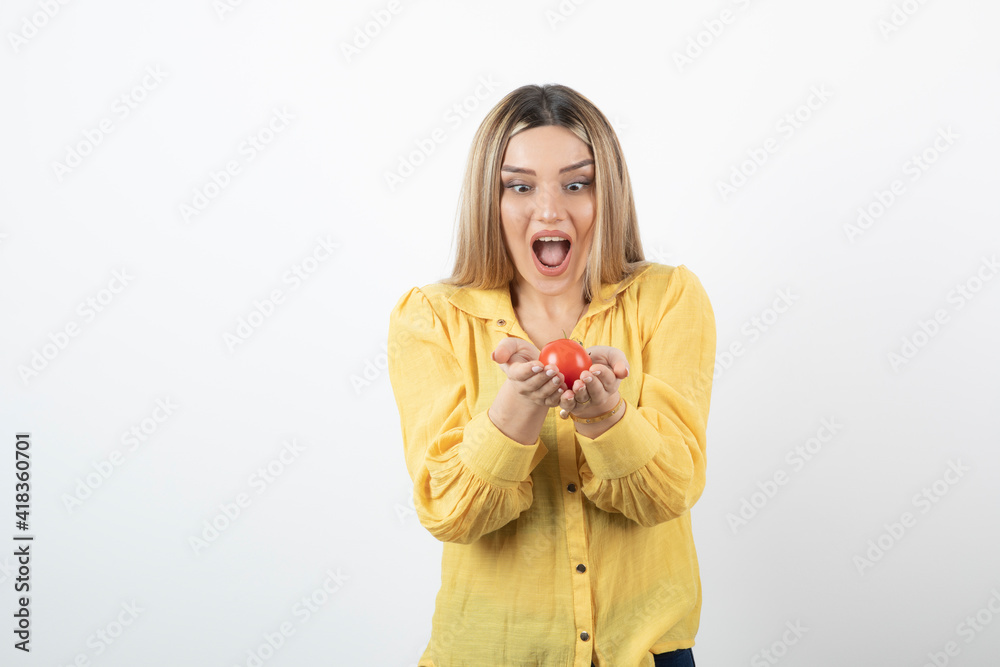 Image of surprised woman looking at red tomato on white background Image of surprised woman looking at red tomato on white background