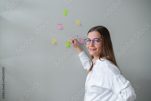Young woman stands against wall and writes on colored stickers. Business planning.