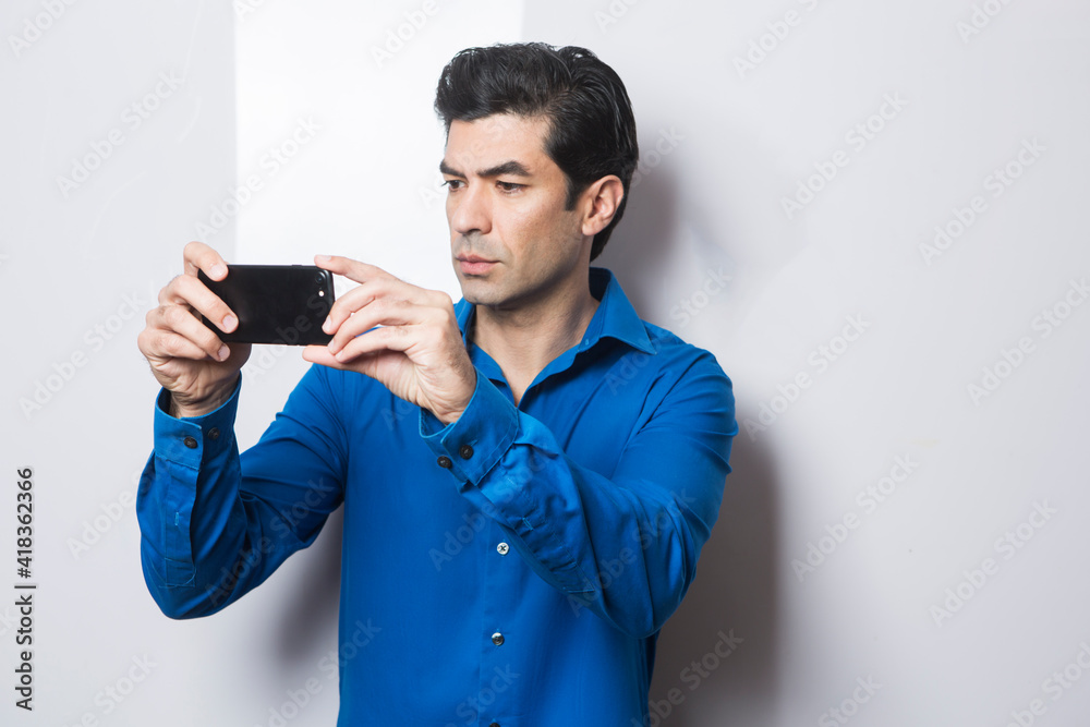 uomo moro in camicia blu fa una foto con il suo smartphone, isolato su sfondo su sfondo bianco uomo moro in camicia blu fa una foto con il suo smartphone, isolato su sfondo su sfondo bianco